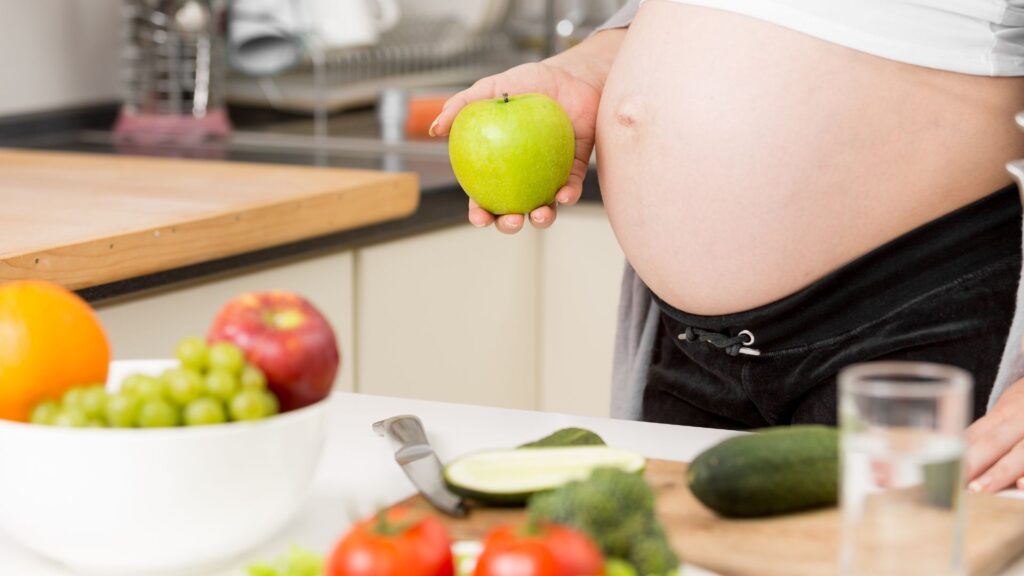Colorful produce like apples, tomatoes, and broccoli on a kitchen counter showing nutritious prenatal foods that support a baby’s growth and maternal health.